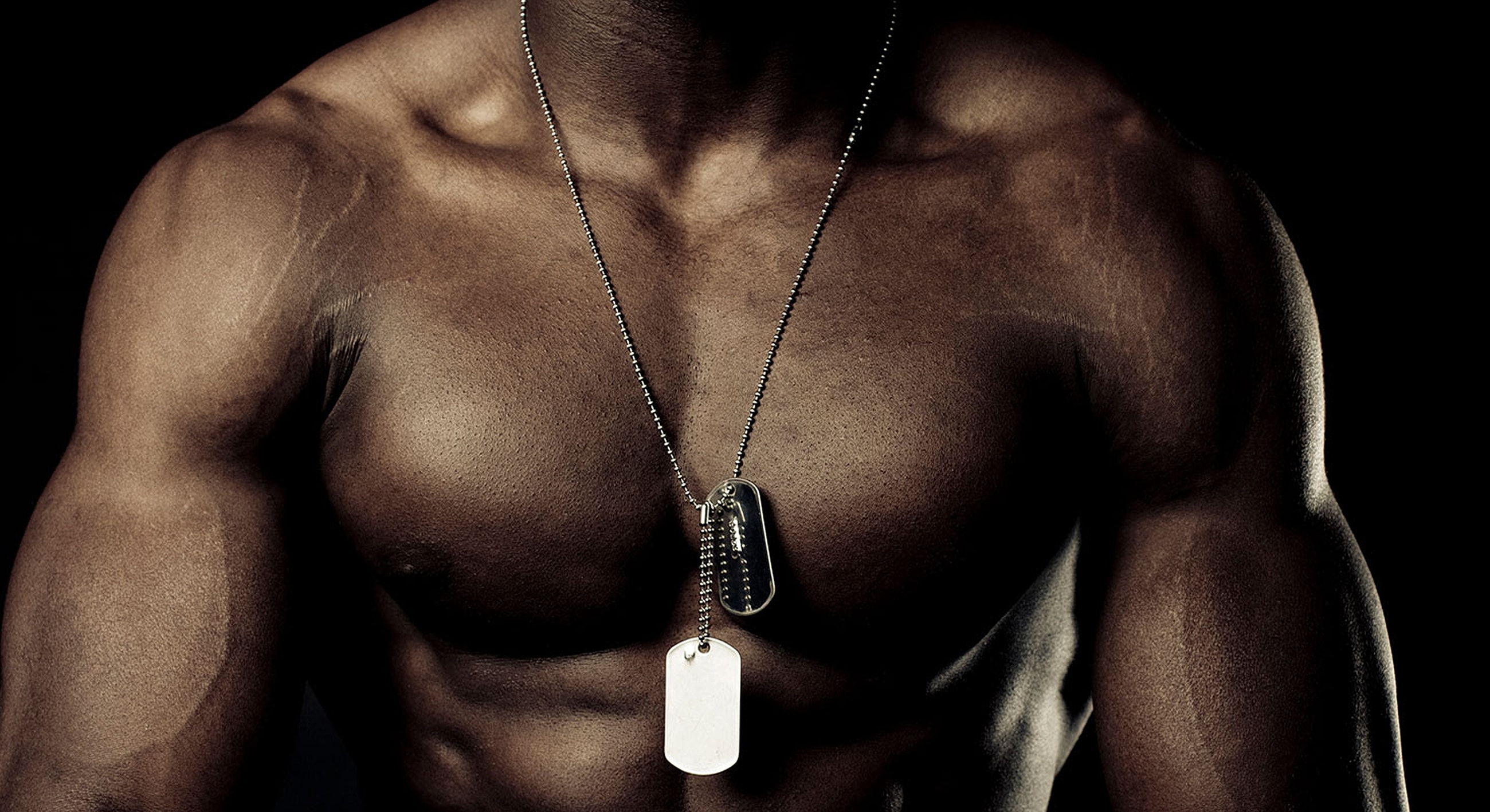Muscular torso with dog tags in dark lighting.